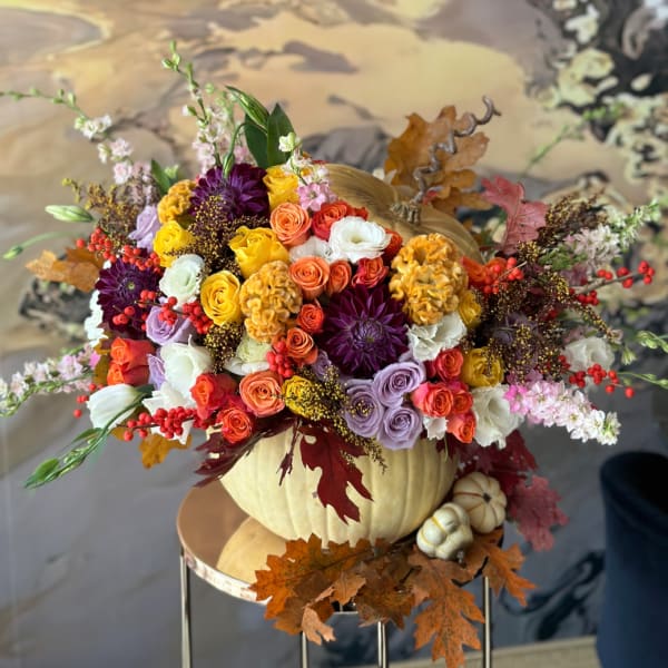 Colorful floral arrangement in a pumpkin container with autumn leaves