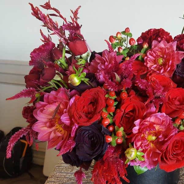 Lush arrangement of red and pink roses and dahlias in a black cylinder vase
