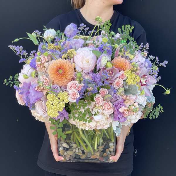 Large pastel bouquet in a clear square vase with pebbles