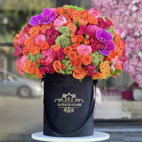 Large bouquet of orange, pink, and purple flowers in a black hatbox