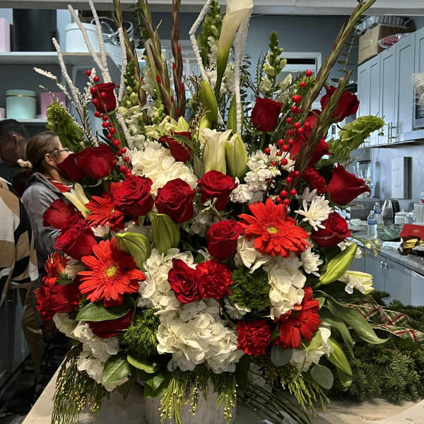 Tall red and white flower arrangement with roses, lilies, and gerbera daisies in a white ceramic vase.