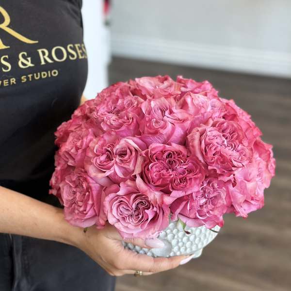 Handheld bouquet of bright pink roses in a white textured vase