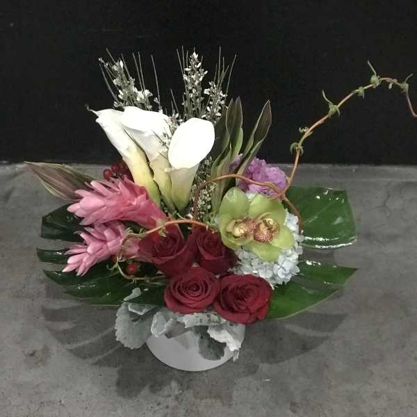 Mixed floral arrangement with white calla lilies, pink blooms, and red roses in a white vase