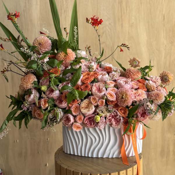 Large peach and pink floral arrangement in a white ribbed vase