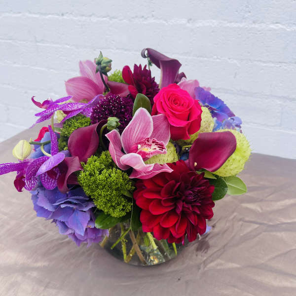 Bright mixed bouquet with pink roses, purple orchids, and burgundy calla lilies in a glass vase