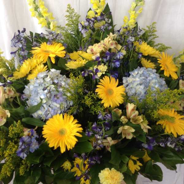 Basket arrangement of yellow daisies, blue hydrangeas, and purple flowers