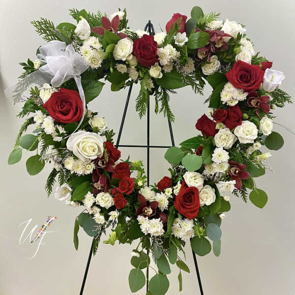 Heart-shaped floral wreath with red and white roses on a black stand