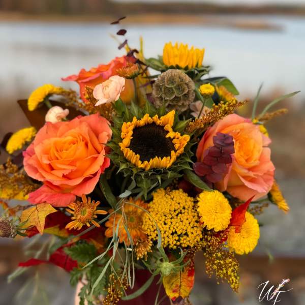 Bouquet with orange roses and a sunflower, held outdoors by water