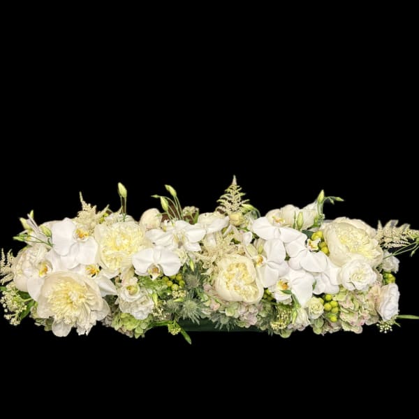 Long white floral arrangement with orchids and pale cream blooms