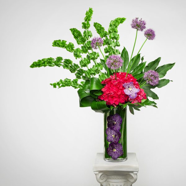Tall modern arrangement with green bells of Ireland, pink hydrangea and purple orchids in a glass vase