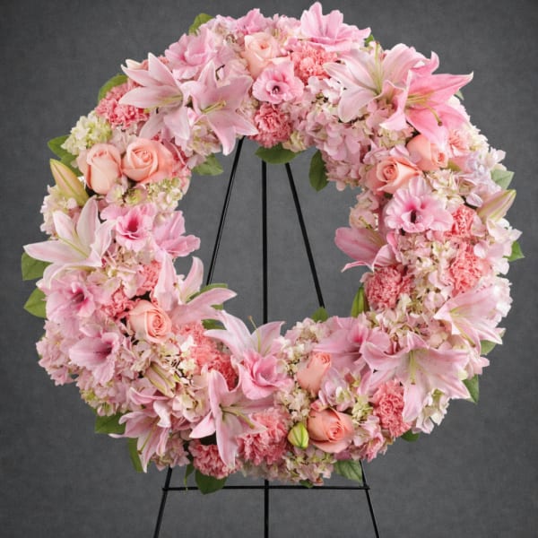 Pink floral wreath with lilies, roses, and carnations on a black stand