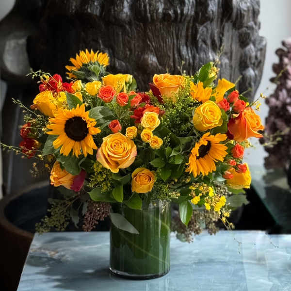 Bouquet of yellow and orange roses with sunflowers in a glass vase