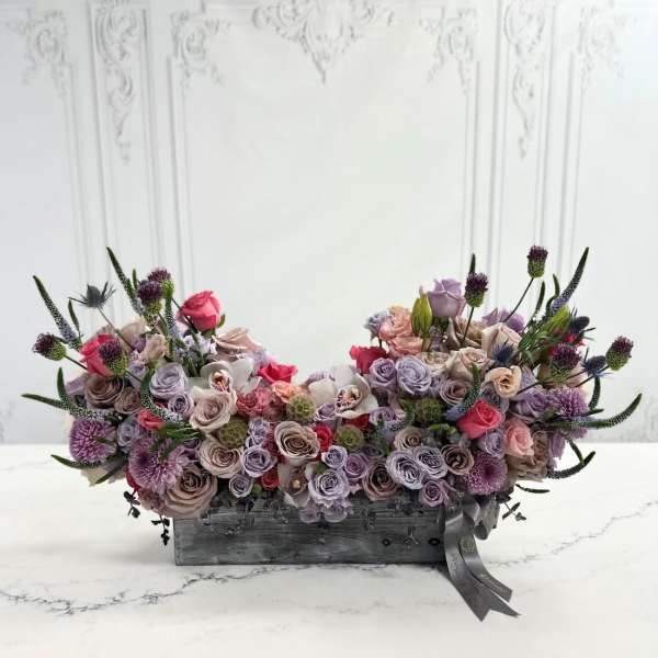 Low floral arrangement of roses and purple blooms in a wooden box