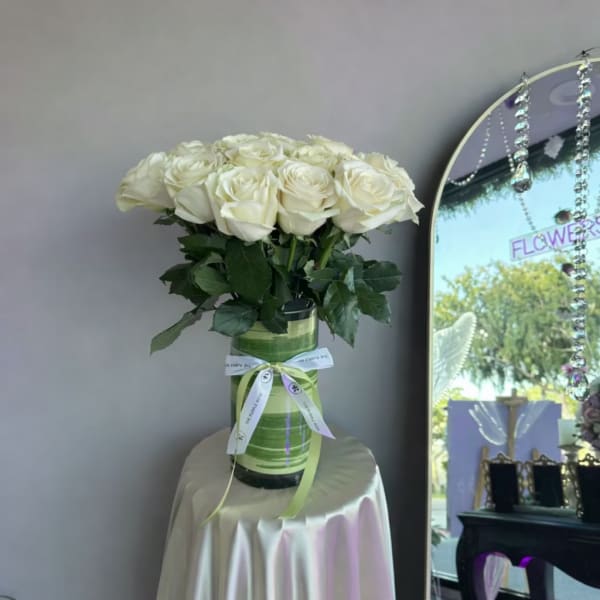 Tall bouquet of white roses in a green-lined glass vase tied with ribbon