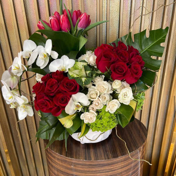 Bouquet of red roses, white orchids, and pink tulips in a white vase