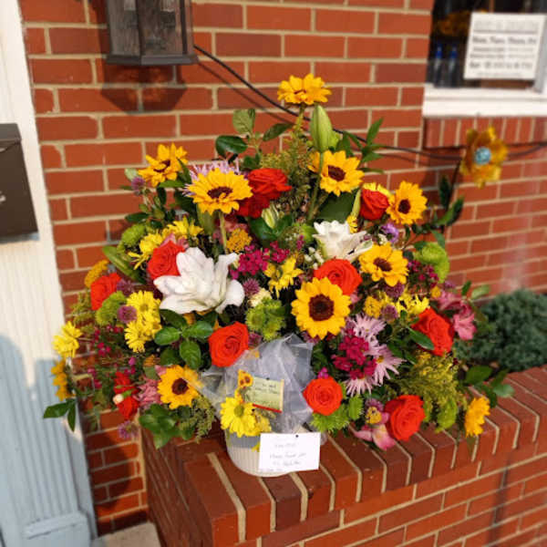 Large mixed bouquet of sunflowers, roses, and lilies in a white container