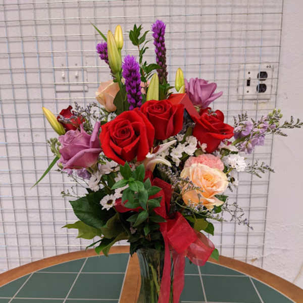Mixed bouquet of red roses, lilies, and purple flowers in a glass vase