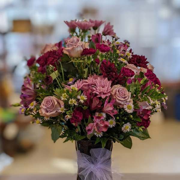 Mixed pink and purple flower arrangement in a dark vase with a lavender bow