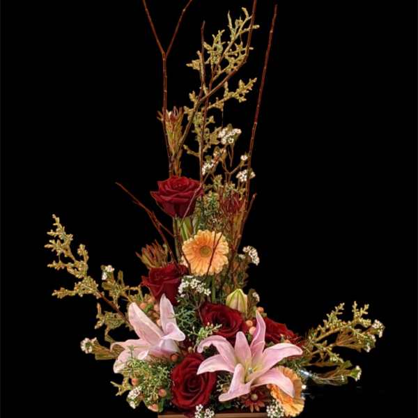 Tall floral arrangement with red roses, pink lilies, and peach daisies