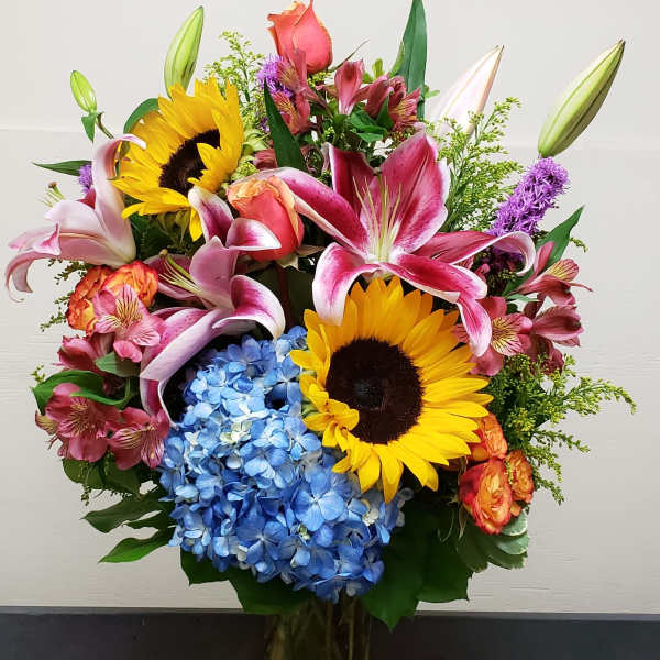 Mixed bouquet with sunflowers, lilies, hydrangeas, and roses in a glass vase