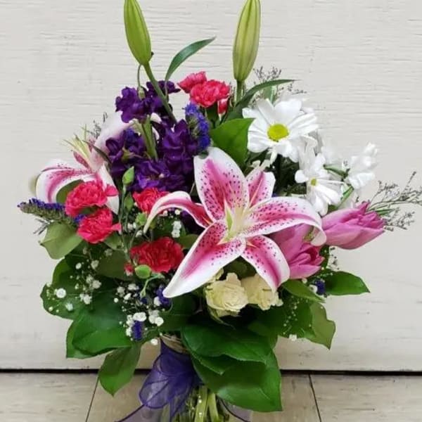 Bouquet of lilies, daisies, carnations, and purple flowers in a glass vase