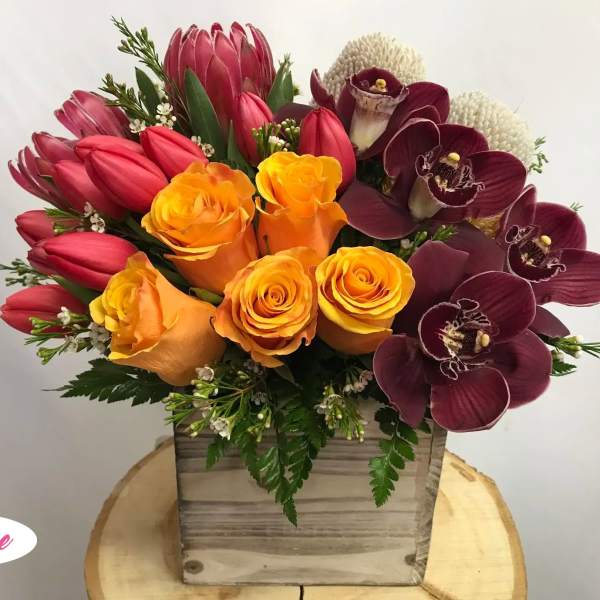 Bouquet of orange roses, red tulips, and burgundy orchids in a wooden box