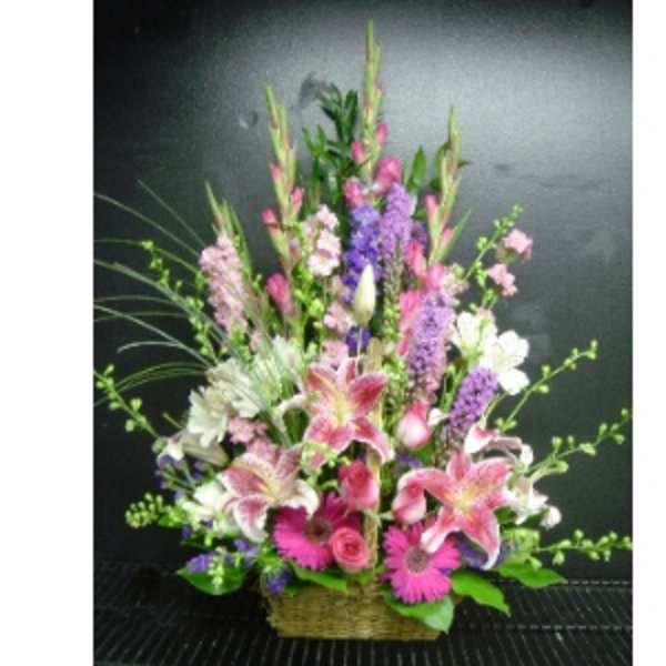 Tall pink and purple mixed flower arrangement in a wicker basket