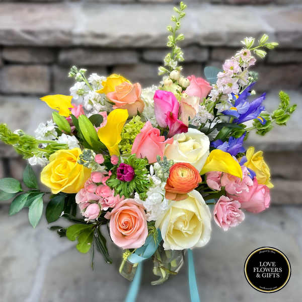 Colorful mixed bouquet of roses, calla lilies, irises and other blooms in a glass vase with ribbon.