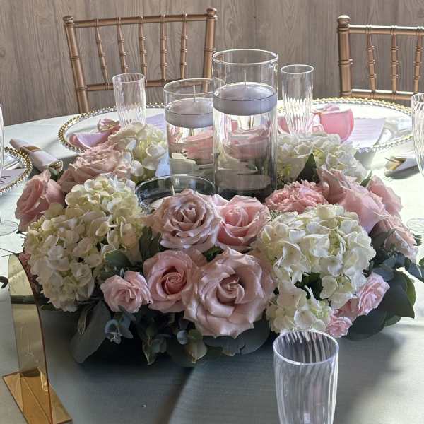 Pink roses and white hydrangeas arranged around glass candle holders on a table