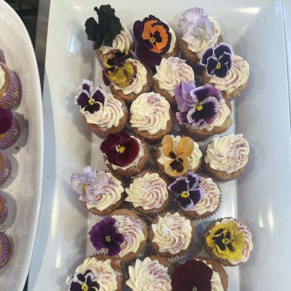 Tray of frosted cupcakes topped with colorful edible flowers