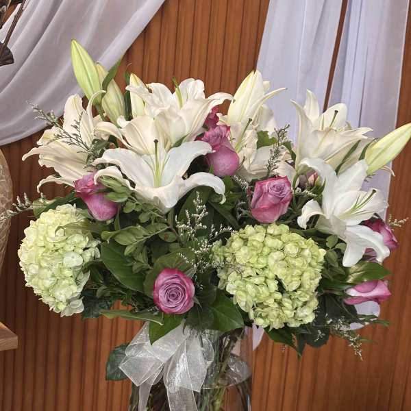 White lilies and pink roses in a glass vase with hydrangeas