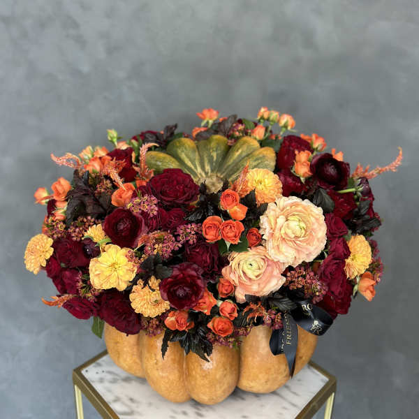 Autumn floral arrangement in a pumpkin-shaped container with red, orange, and yellow blooms