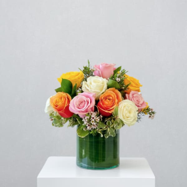 Mixed bouquet of yellow, orange, pink, and white roses arranged in a green glass cylinder vase