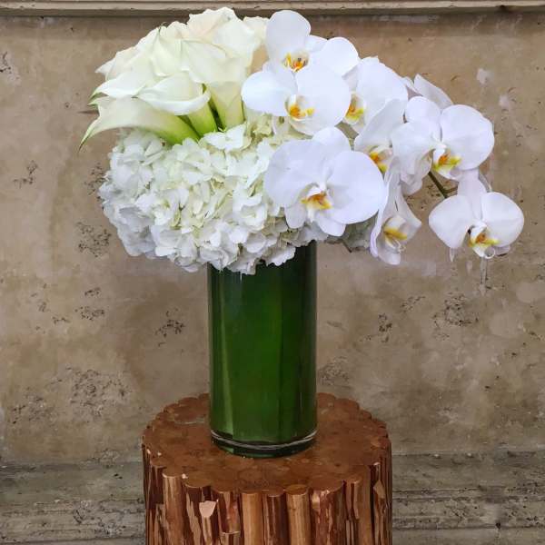 White floral arrangement with orchids, hydrangeas, and calla lilies in a green vase