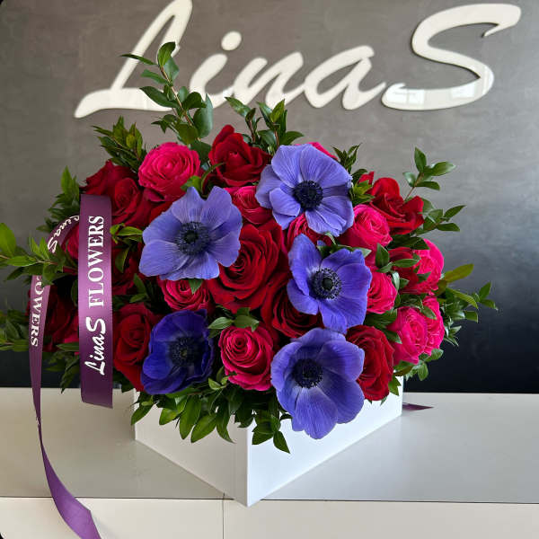 Bouquet of red and pink roses with purple anemones in a white box