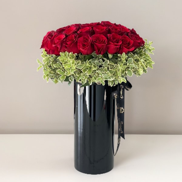 Red roses arranged in a black vase with variegated greenery
