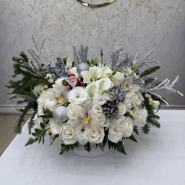 White floral arrangement with holiday ornaments and evergreen accents in a low container