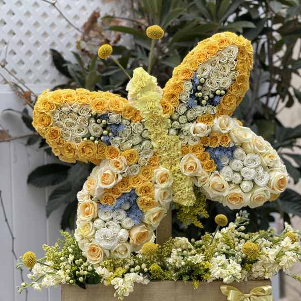 Butterfly-shaped floral arrangement of yellow and white roses with blue accents