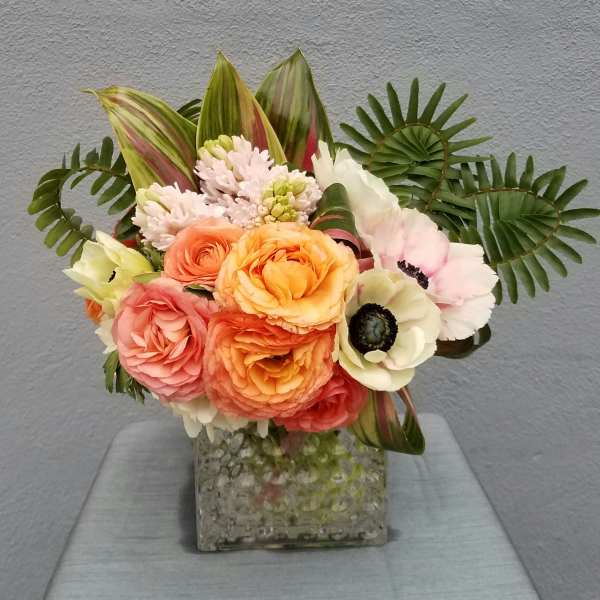 Mixed bouquet of peach, pink, and white flowers in a square glass vase