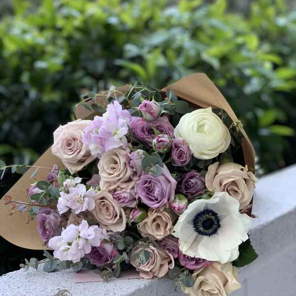 Bouquet of blush, lavender, and white flowers wrapped in brown paper
