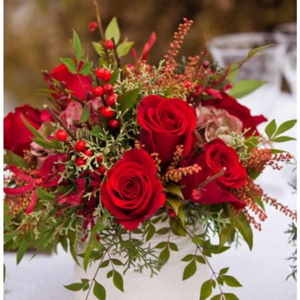 Red roses arranged in a white vase with trailing greenery