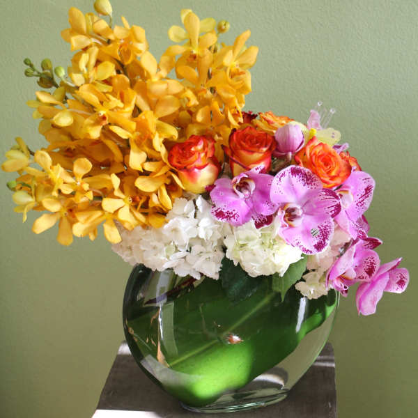 Yellow orchids, pink orchids, roses, and white hydrangeas in a glass vase