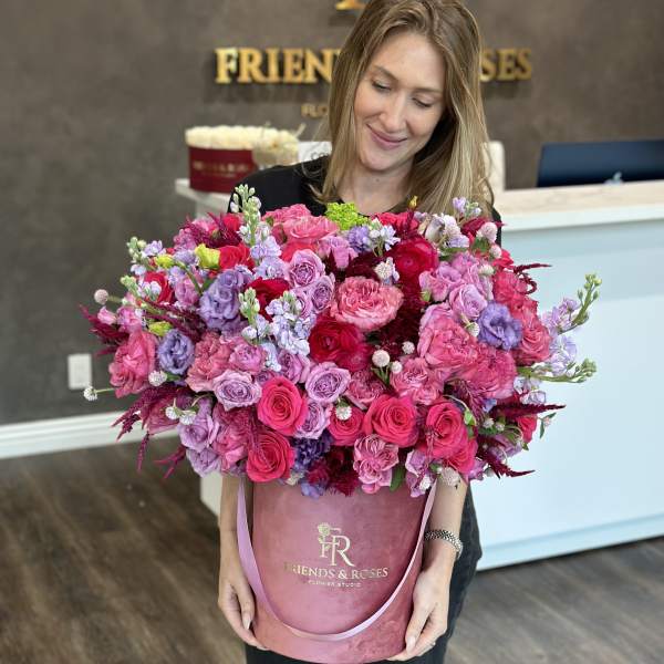 Woman holding a large pink and purple rose arrangement in a velvet hat box