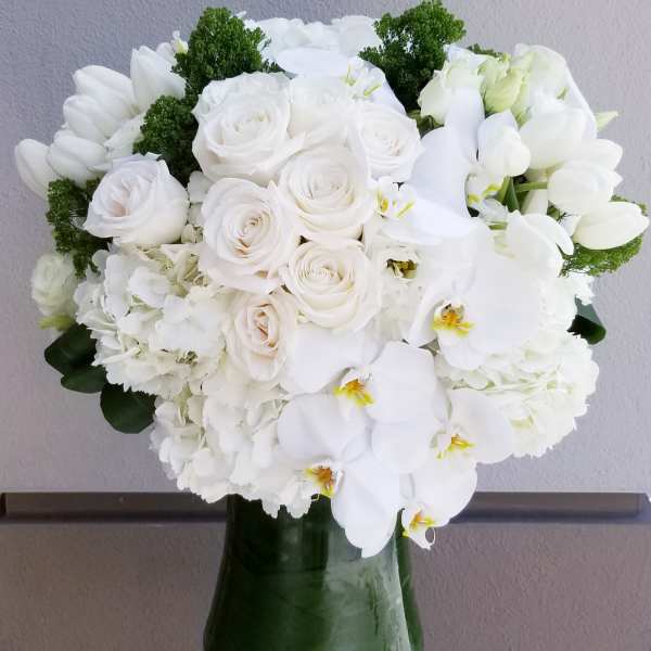 White rose and orchid bouquet in a green glass vase