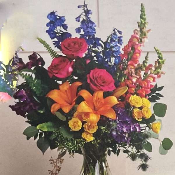 Colorful bouquet with roses, lilies, and tall blue and pink spikes in a glass vase