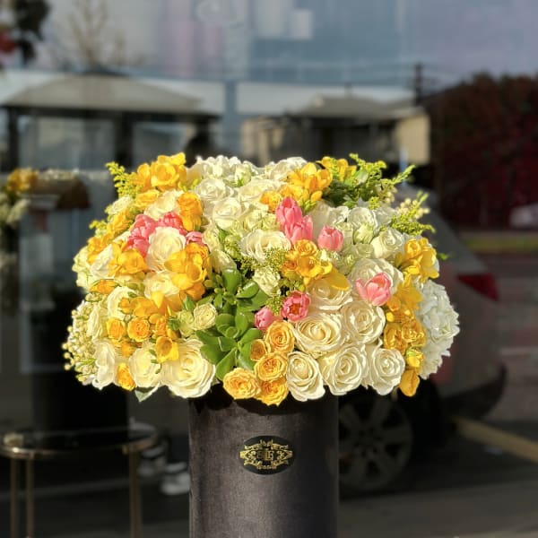 Large bouquet of white, yellow, and pink roses in a black hat box