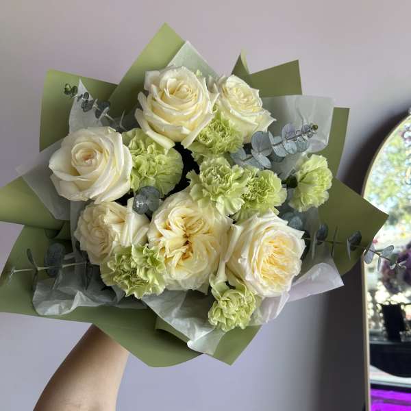 Hand-tied bouquet of cream roses and pale green carnations wrapped in green and white paper