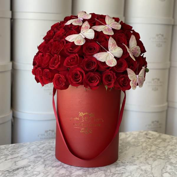 Red rose arrangement in a red hatbox with butterfly accents