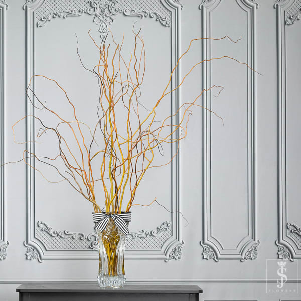 Tall glass vase with curly orange branches and a striped ribbon