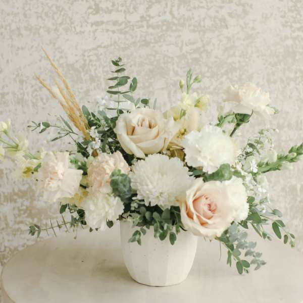 Low arrangement of cream roses, white mums, and peach carnations in a white pot